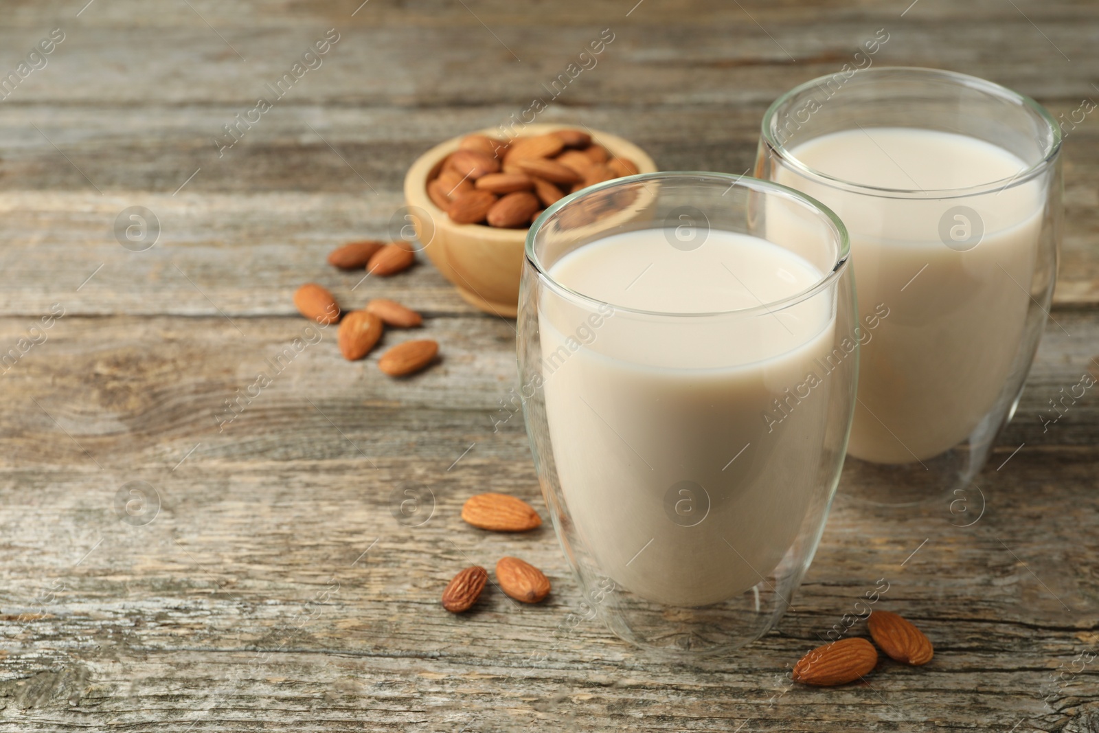 Photo of Fresh nut milk in glasses and almonds on wooden table, closeup. Space for text