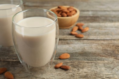 Photo of Fresh nut milk in glasses and almonds on wooden table, closeup. Space for text