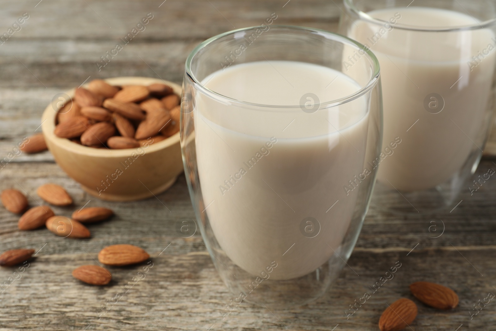 Photo of Fresh nut milk in glasses and almonds on wooden table, closeup