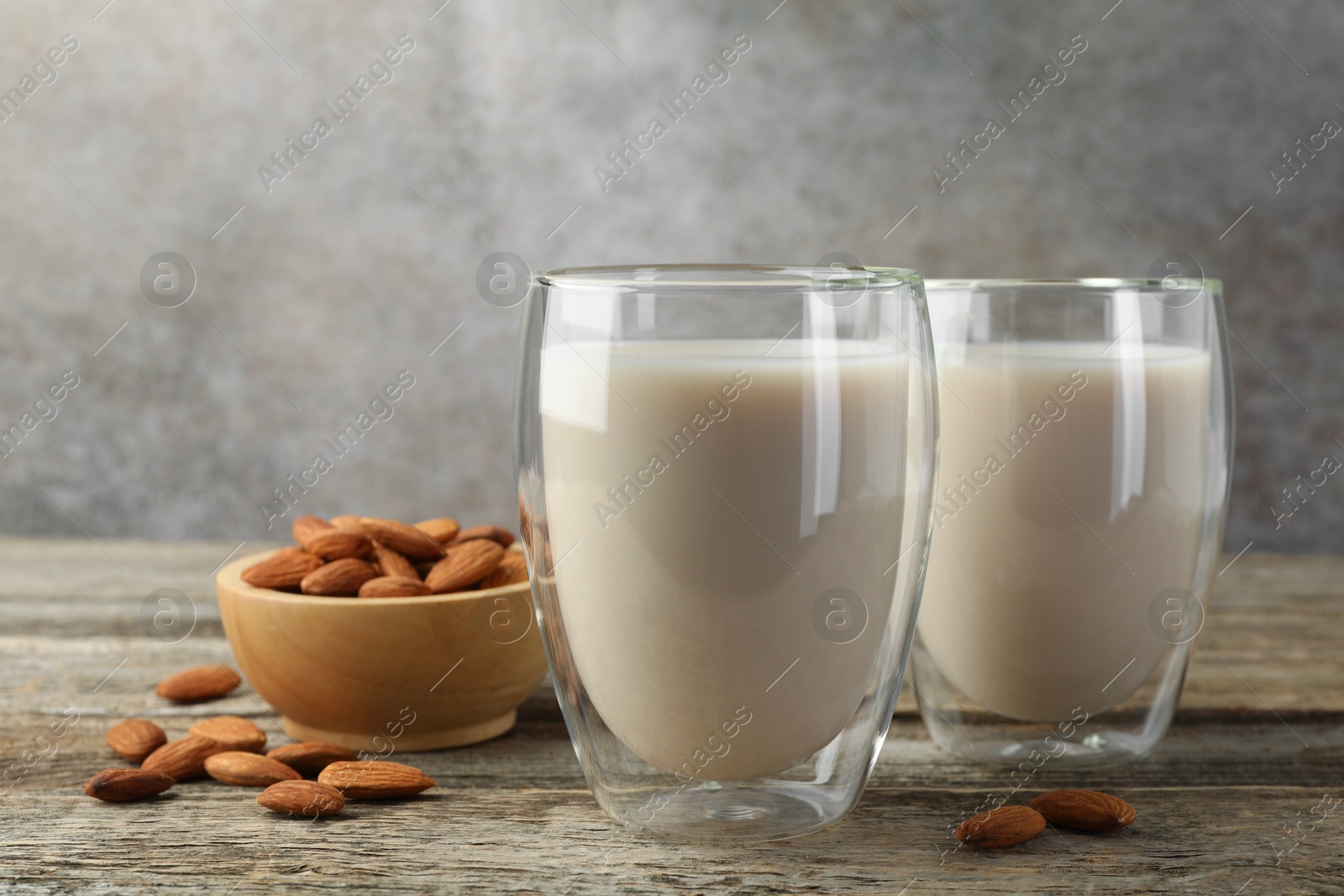 Photo of Fresh nut milk in glasses and almonds on wooden table, closeup