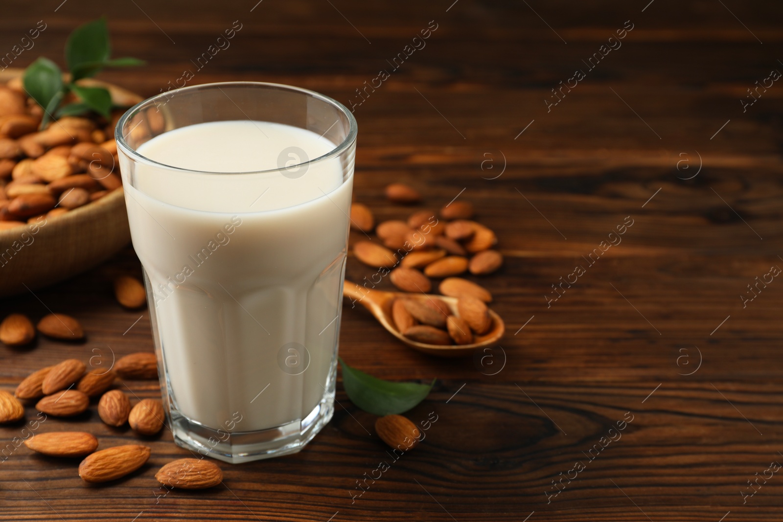 Photo of Fresh almond milk in glass and nuts on wooden table, closeup. Space for text