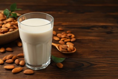 Fresh almond milk in glass and nuts on wooden table, closeup. Space for text