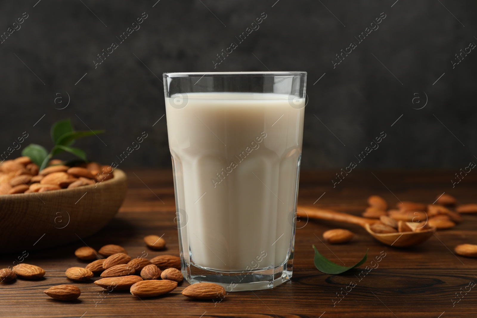 Photo of Fresh almond milk in glass and nuts on wooden table