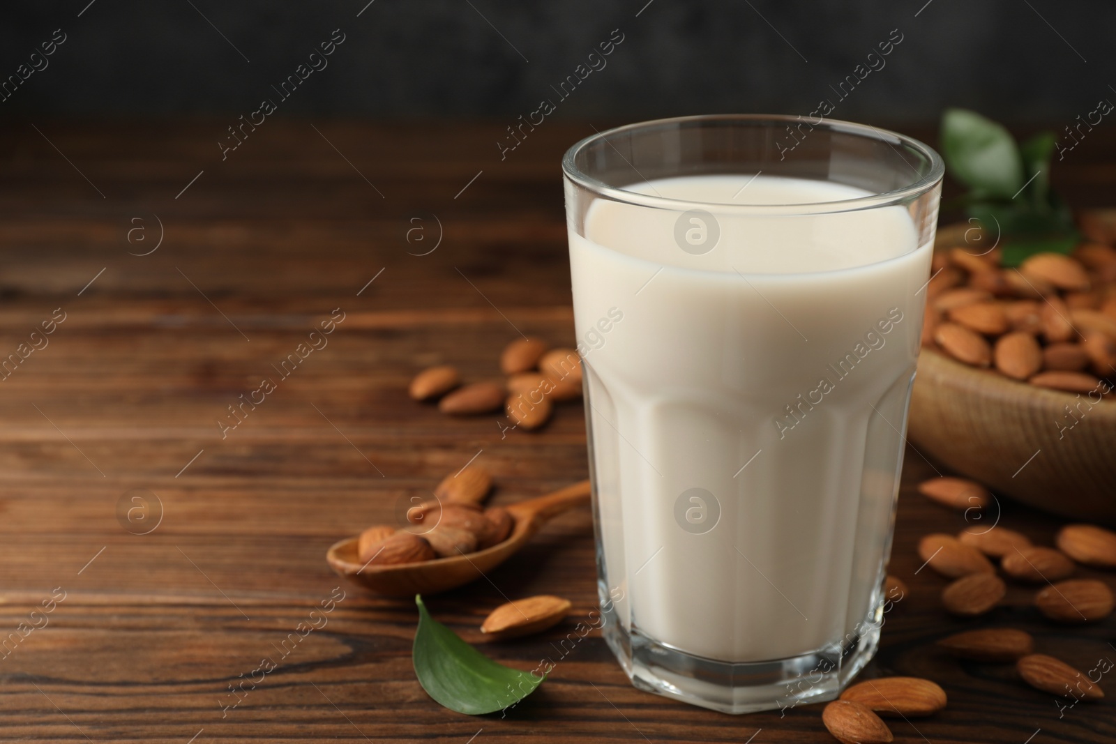 Photo of Fresh almond milk in glass and nuts on wooden table, closeup. Space for text