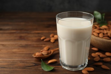 Fresh almond milk in glass and nuts on wooden table, closeup. Space for text