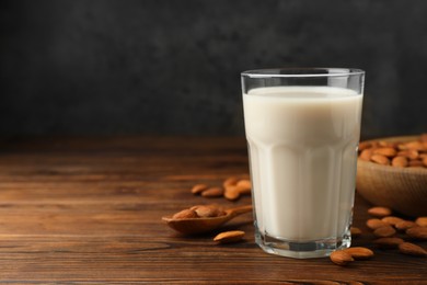 Photo of Fresh almond milk in glass and nuts on wooden table, space for text