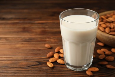 Photo of Fresh almond milk in glass and nuts on wooden table, closeup. Space for text