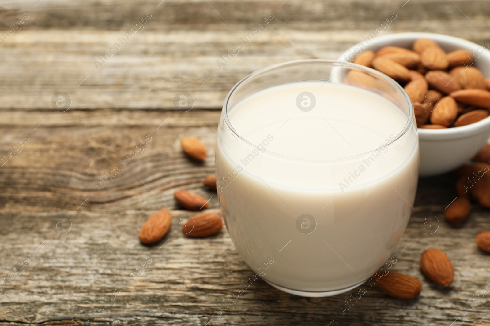 Photo of Fresh almond milk in glass and nuts on wooden table, closeup