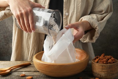 Making almond milk. Woman pouring nut mixture into cheesecloth at wooden table, closeup