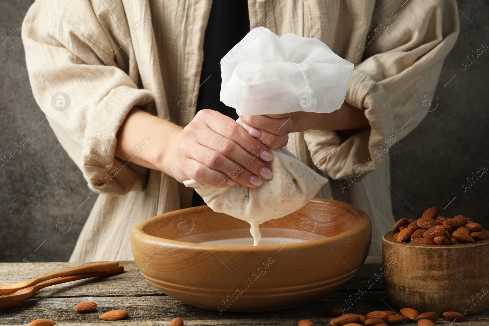 Photo of Woman making almond milk at wooden table, closeup