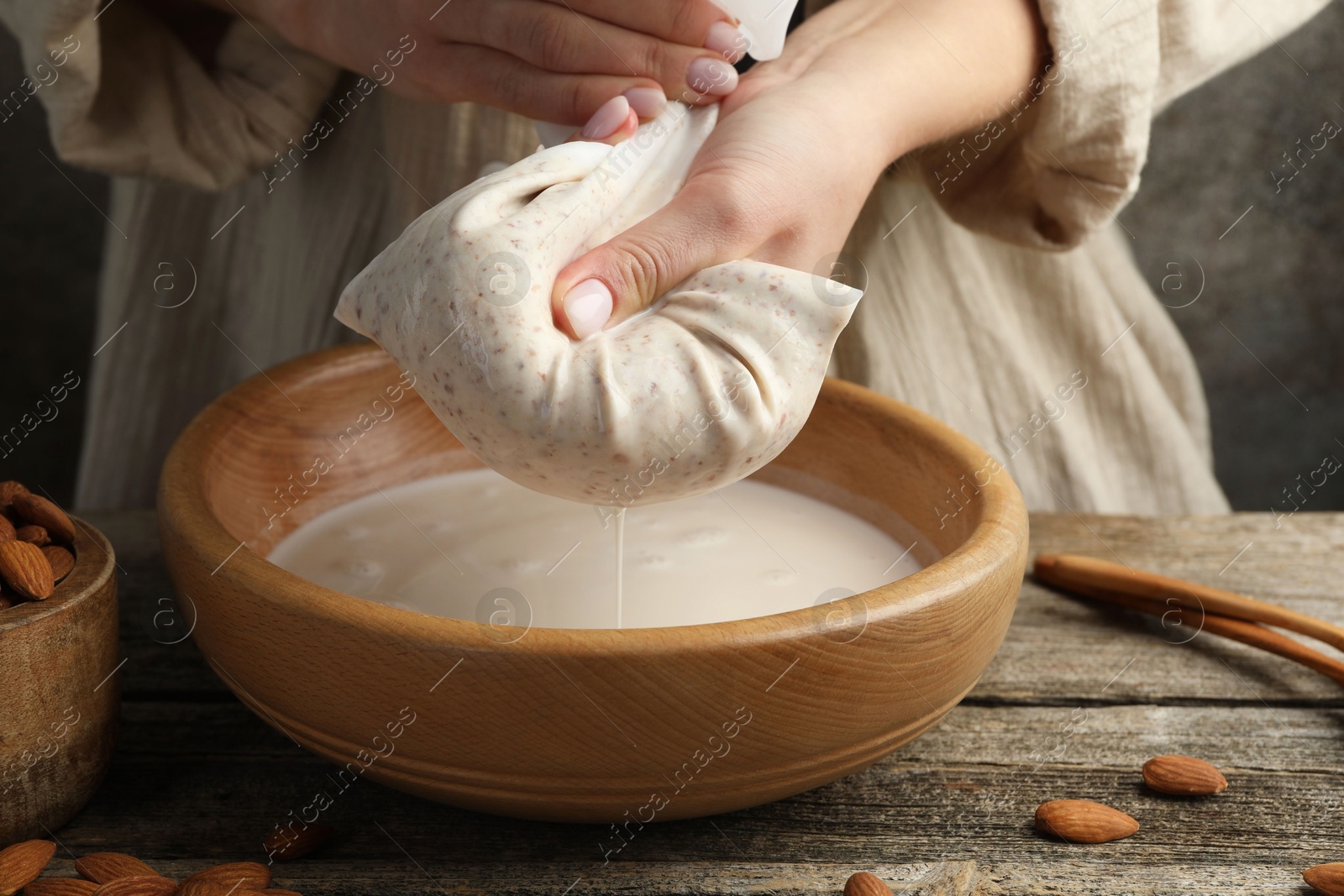 Photo of Woman making almond milk at wooden table, closeup