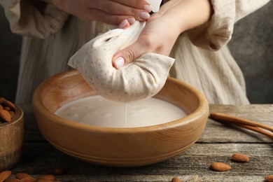 Photo of Woman making almond milk at wooden table, closeup