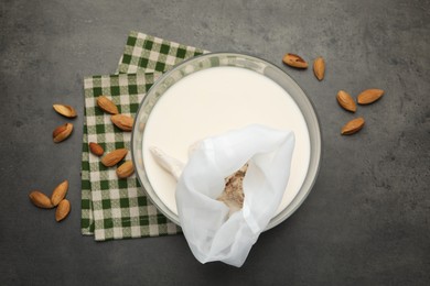 Photo of Homemade almond milk, cheesecloth with mixture and nuts on black table, top view