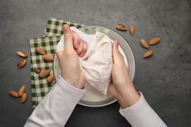 Photo of Woman making almond milk and nuts at black table, top view