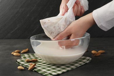 Woman making almond milk and nuts at black table, closeup