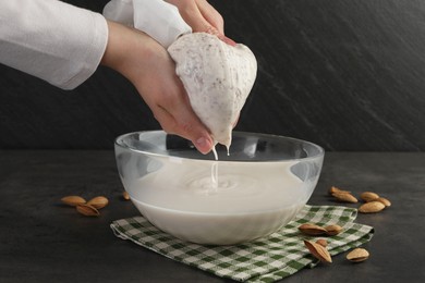 Photo of Woman making almond milk and nuts at black table, closeup