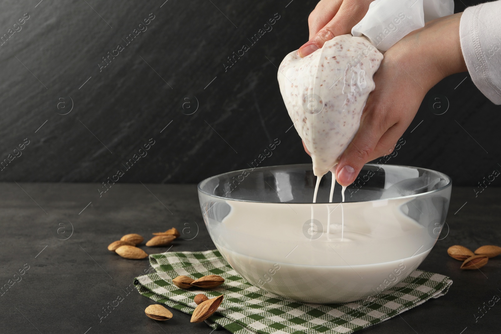 Photo of Woman making almond milk and nuts at black table, closeup