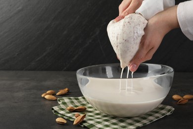 Photo of Woman making almond milk and nuts at black table, closeup