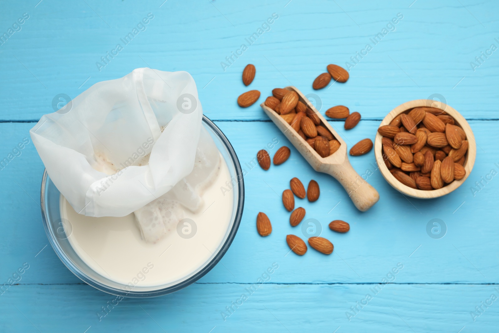 Photo of Homemade almond milk, cheesecloth with mixture and nuts on light blue wooden table, top view