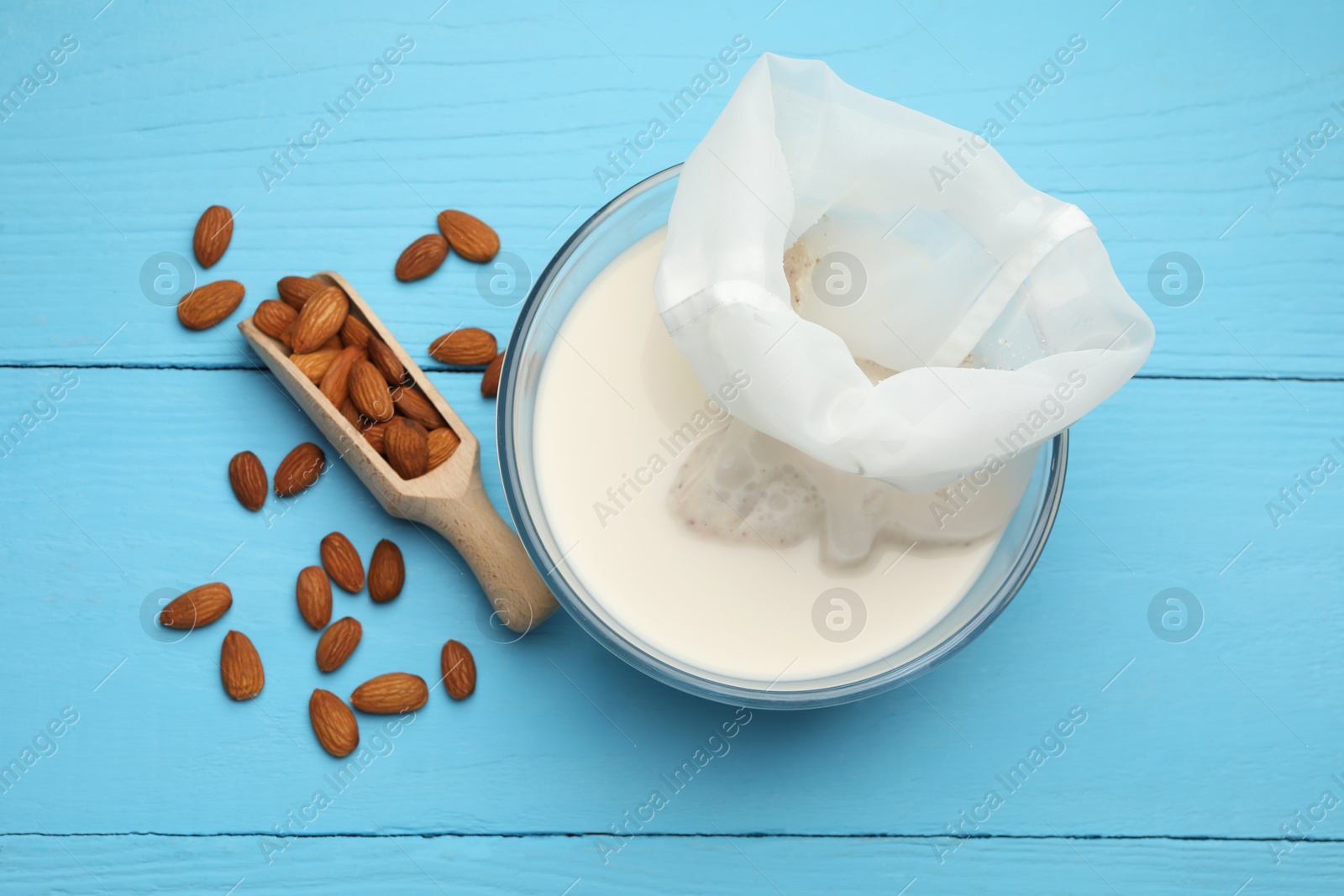 Photo of Homemade almond milk, cheesecloth with mixture and nuts on light blue wooden table, top view