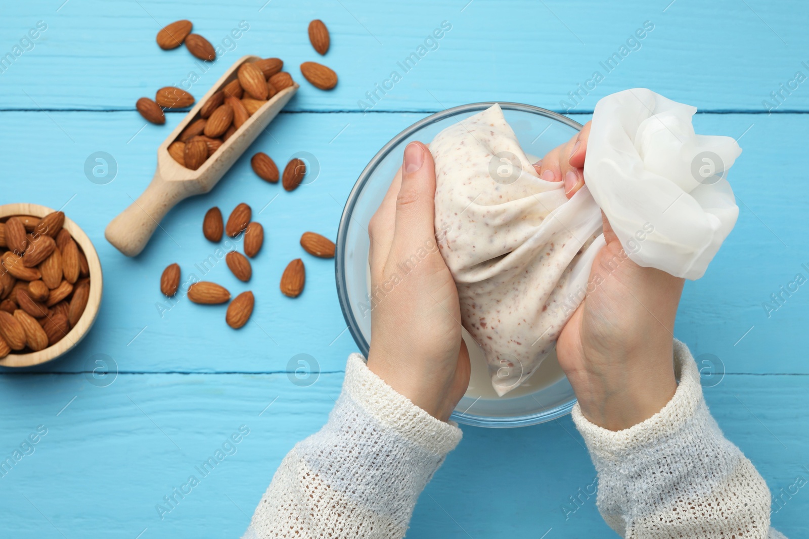 Photo of Woman making almond milk and nuts at light blue wooden table, top view