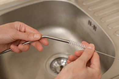 Photo of Woman cleaning metal drinking straw with brush in kitchen, closeup