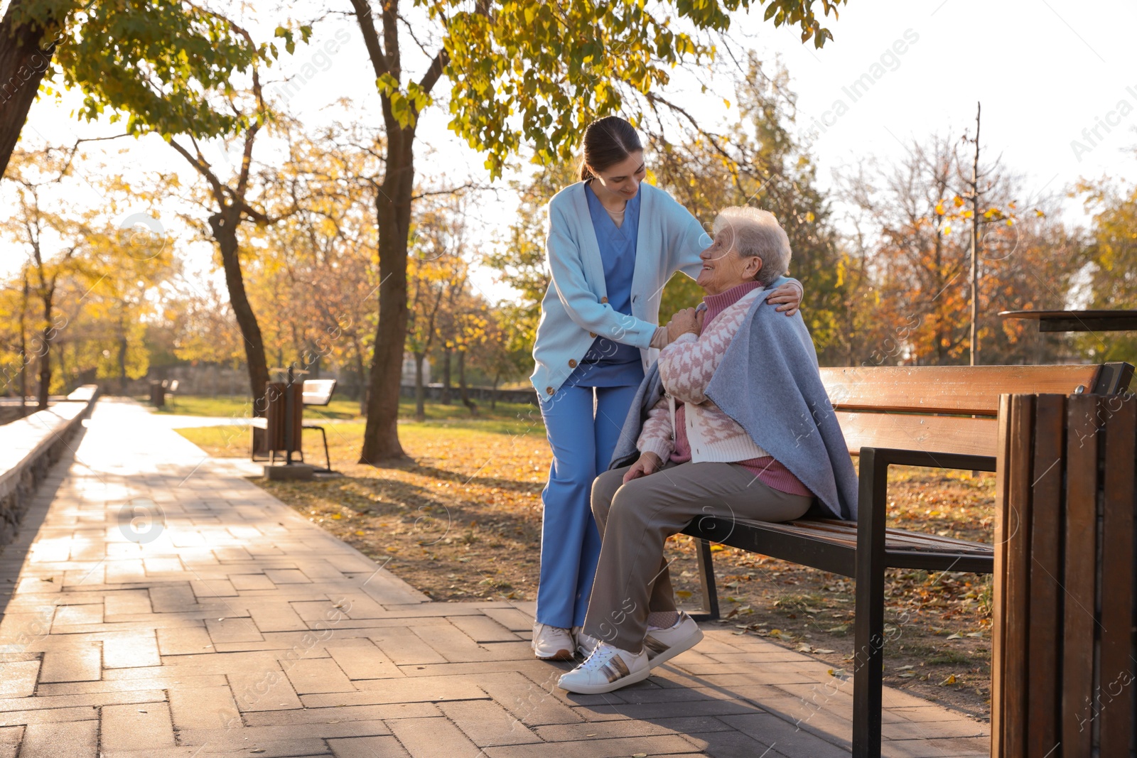 Photo of Elderly woman with her caregiver in park. Space for text