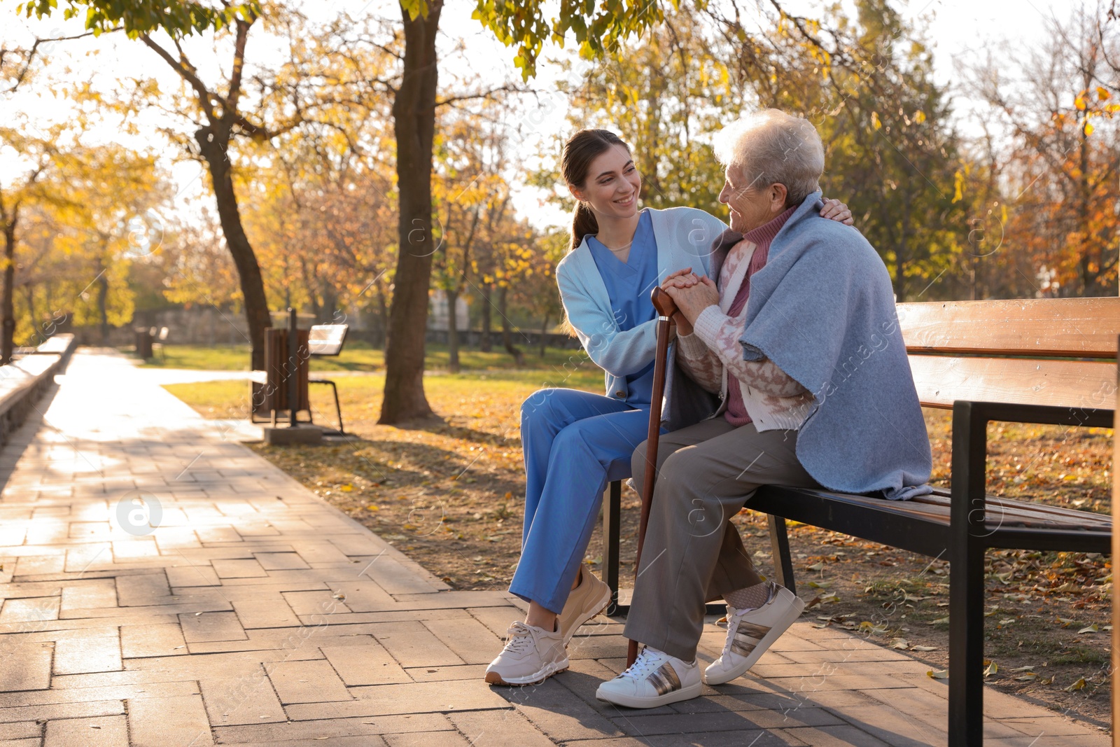 Photo of Elderly woman with walking cane and her caregiver in park. Space for text