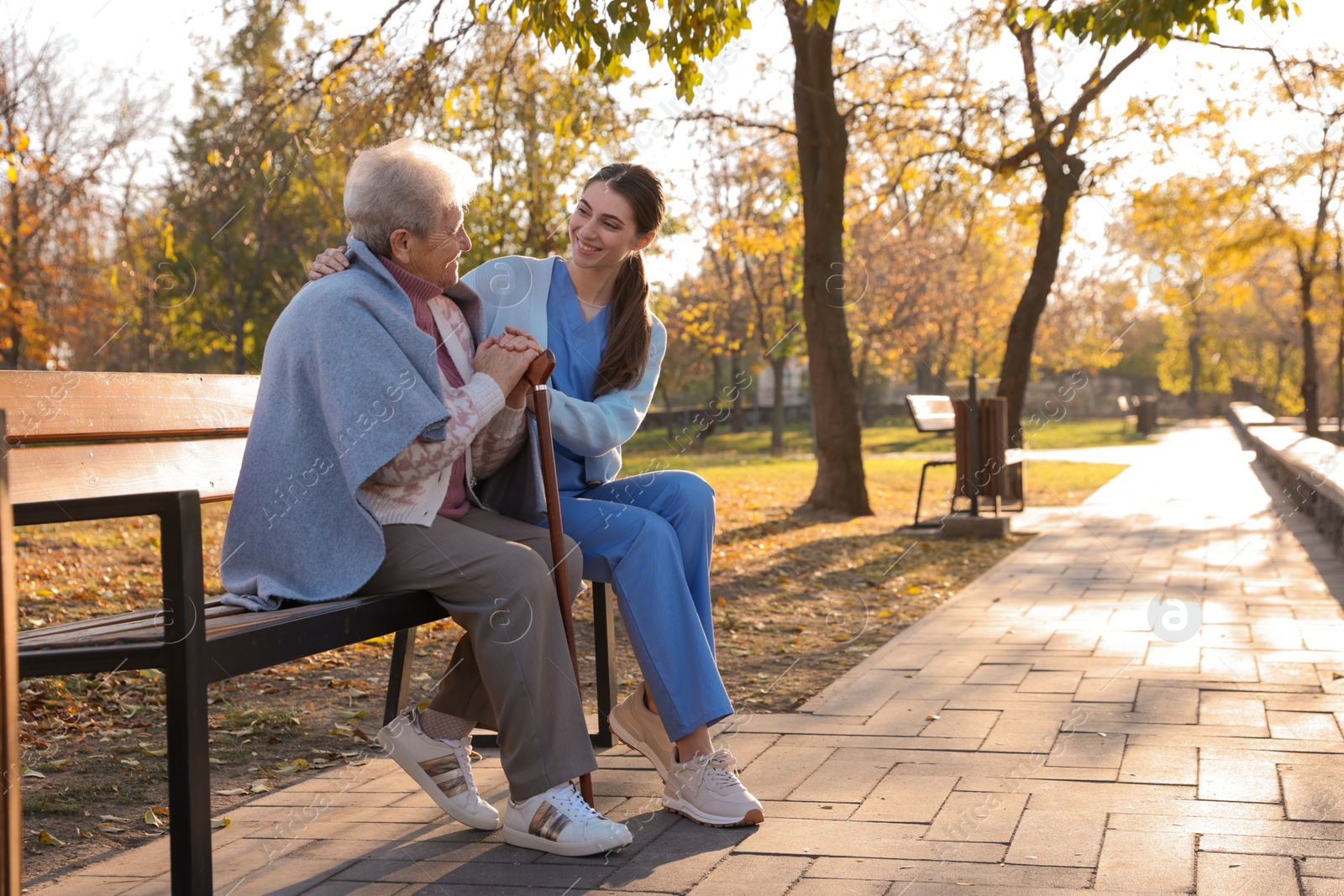 Photo of Elderly woman with walking cane and her caregiver in park. Space for text