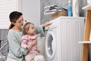 Photo of Housewife with her little daughter doing laundry at home