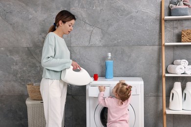 Housewife with her little daughter doing laundry at home