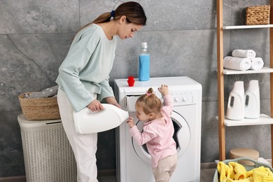 Photo of Housewife with her little daughter doing laundry at home