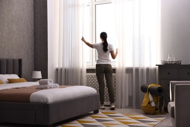 Photo of Traveller opening curtains in hotel room, back view