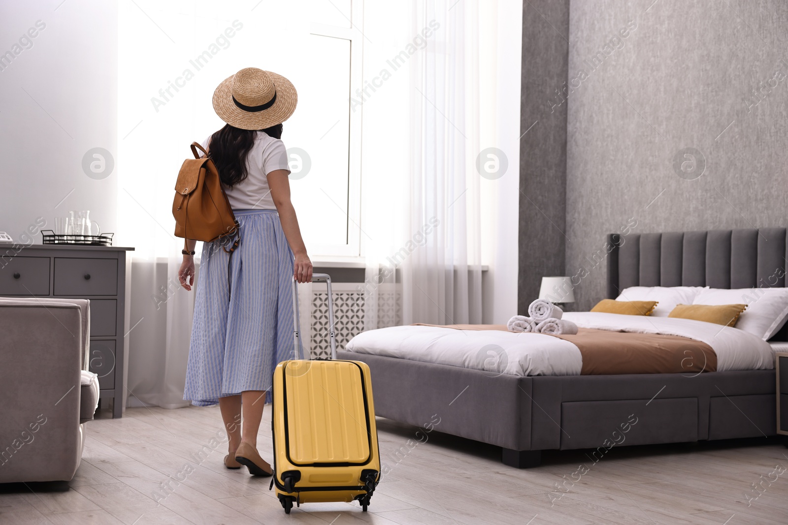 Photo of Traveller with suitcase in hotel room, back view