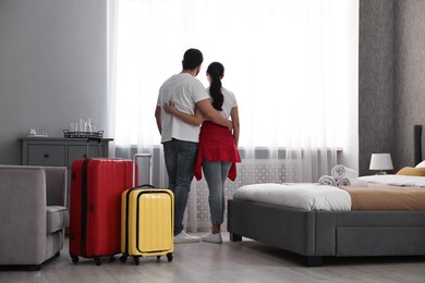 Photo of Travellers with suitcases standing near window in hotel room, back view