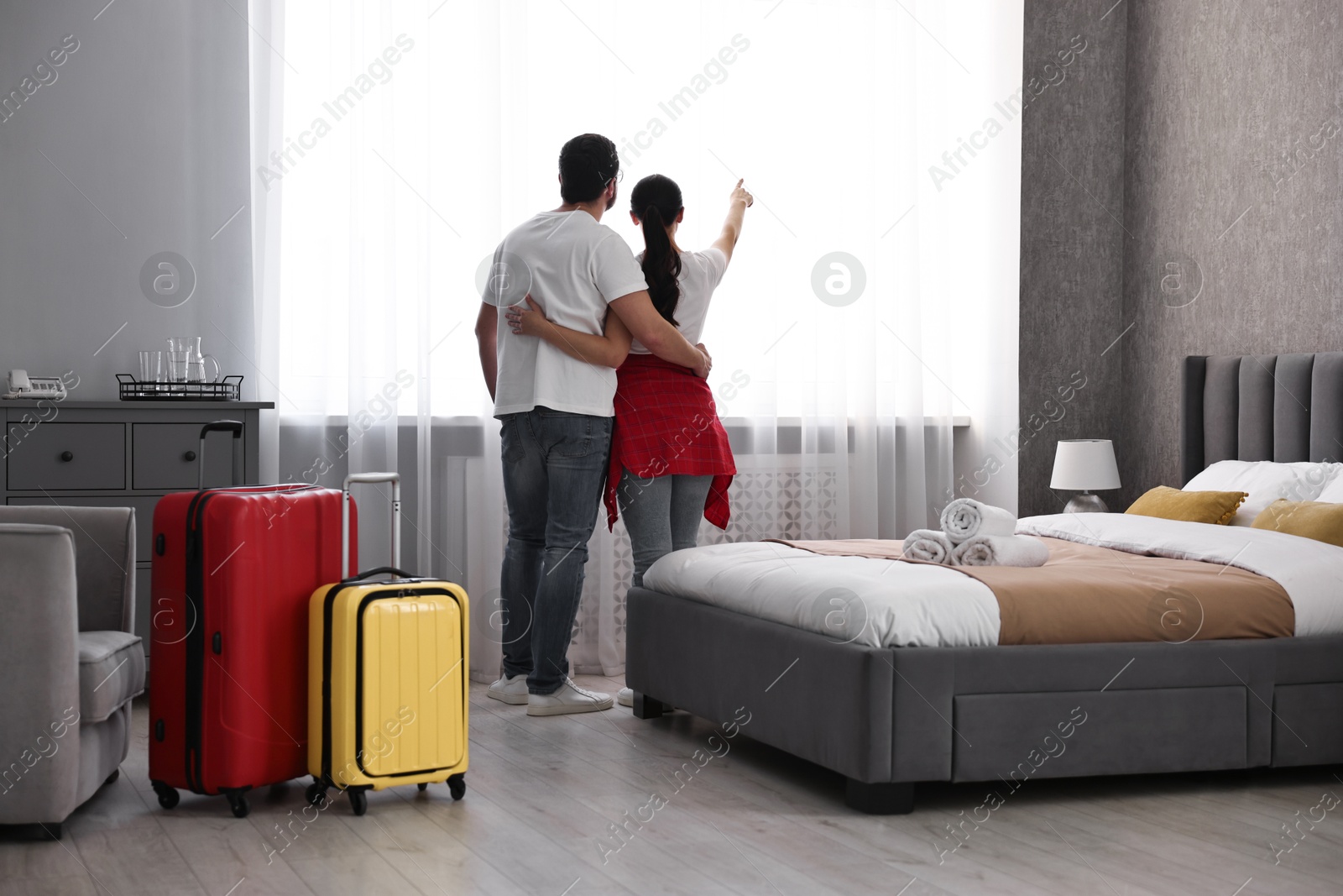 Photo of Travellers with suitcases standing near window in hotel room, back view