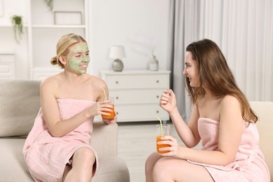 Photo of Spa day. Beautiful women with face masks and healthy drinks on sofa indoors