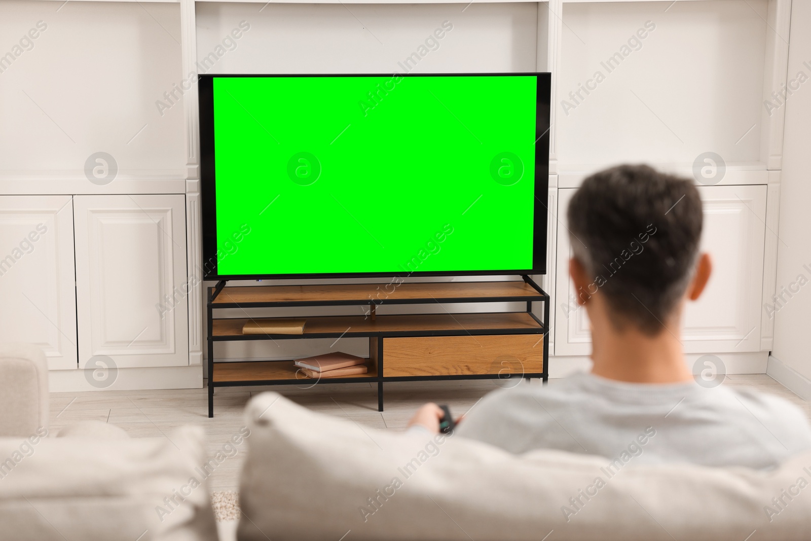 Photo of Man watching TV on sofa at home, back view