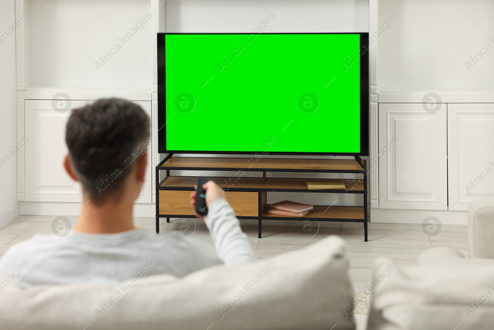 Photo of Man watching TV on sofa at home, back view