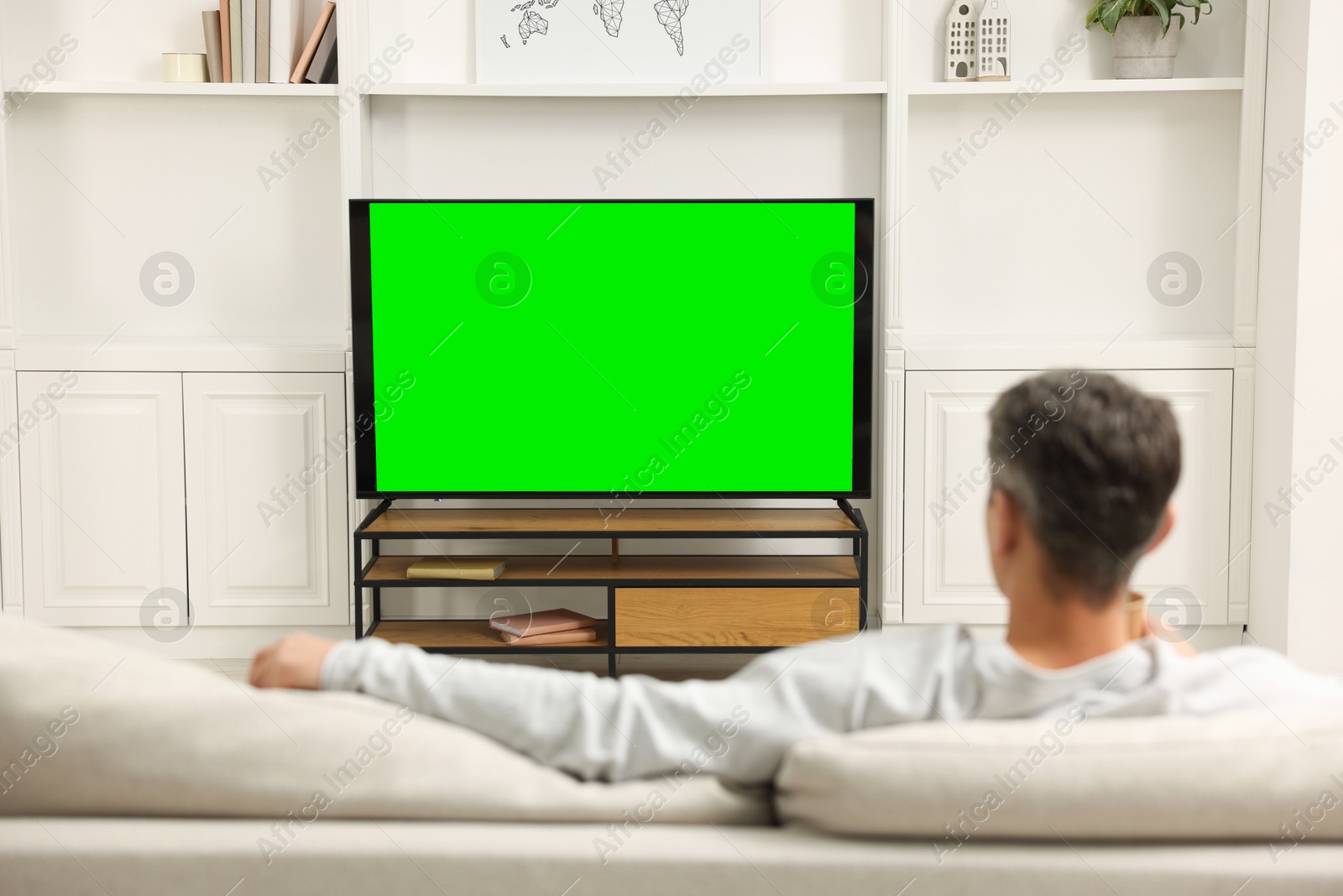 Photo of Man watching TV on sofa at home, back view