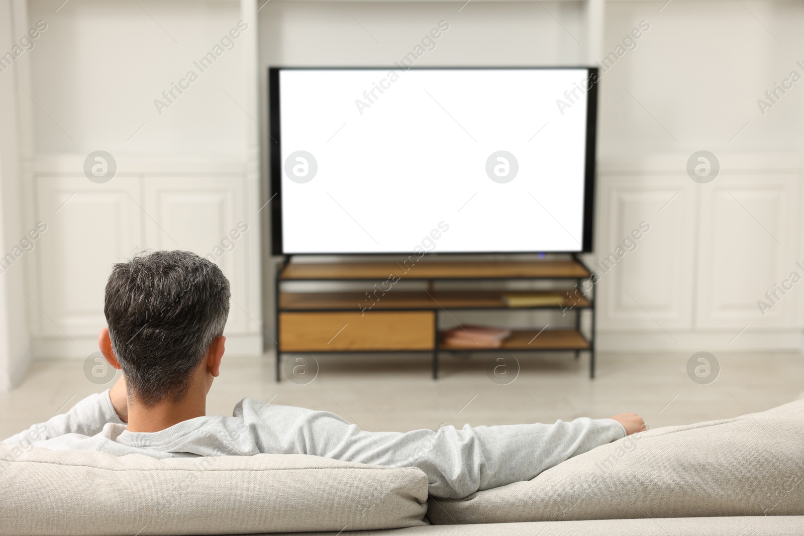 Photo of Man watching TV on sofa at home, back view