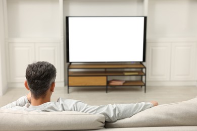 Photo of Man watching TV on sofa at home, back view