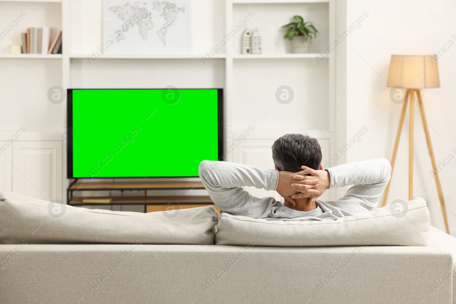 Photo of Man watching TV on sofa at home, back view