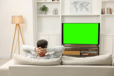 Photo of Man watching TV on sofa at home, back view