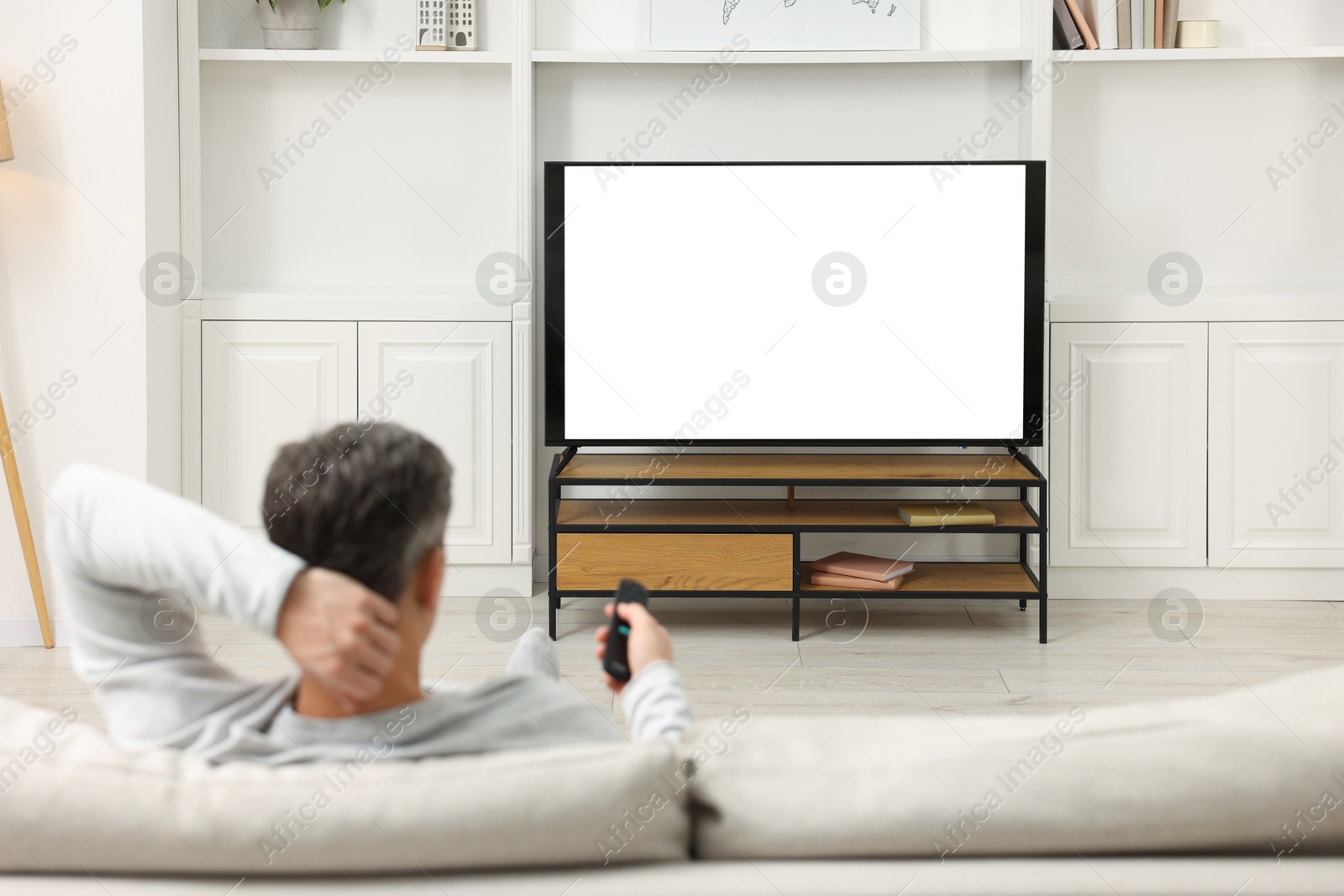 Photo of Man watching TV on sofa at home, back view