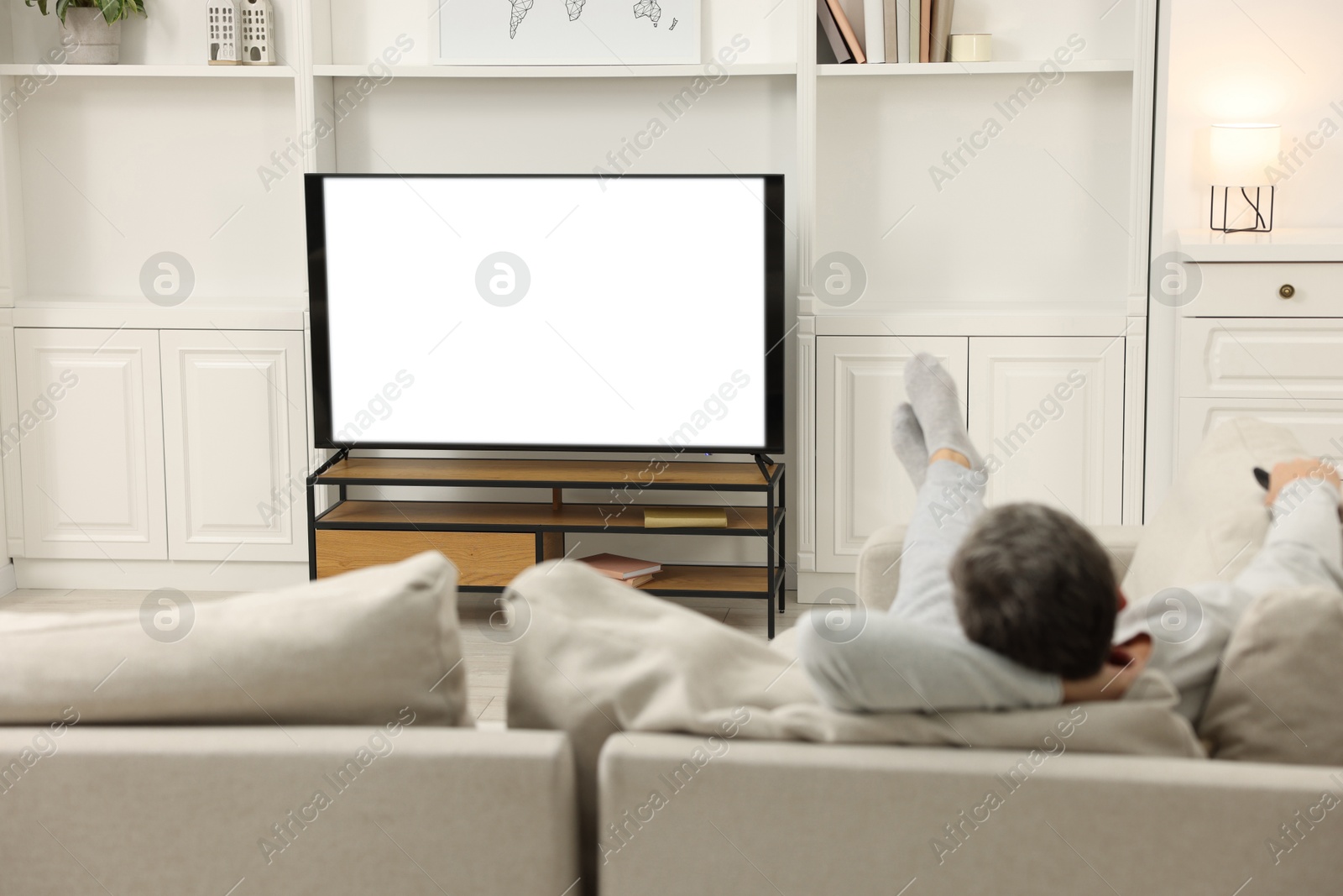 Photo of Man watching TV on sofa at home, back view