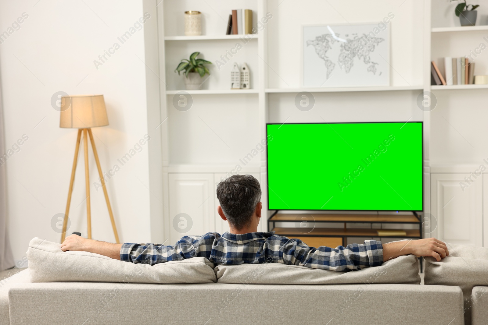 Photo of Man watching TV on sofa at home, back view