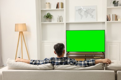 Photo of Man watching TV on sofa at home, back view