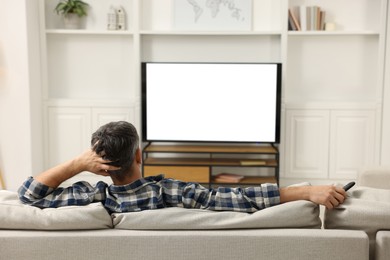 Photo of Man watching TV on sofa at home, back view