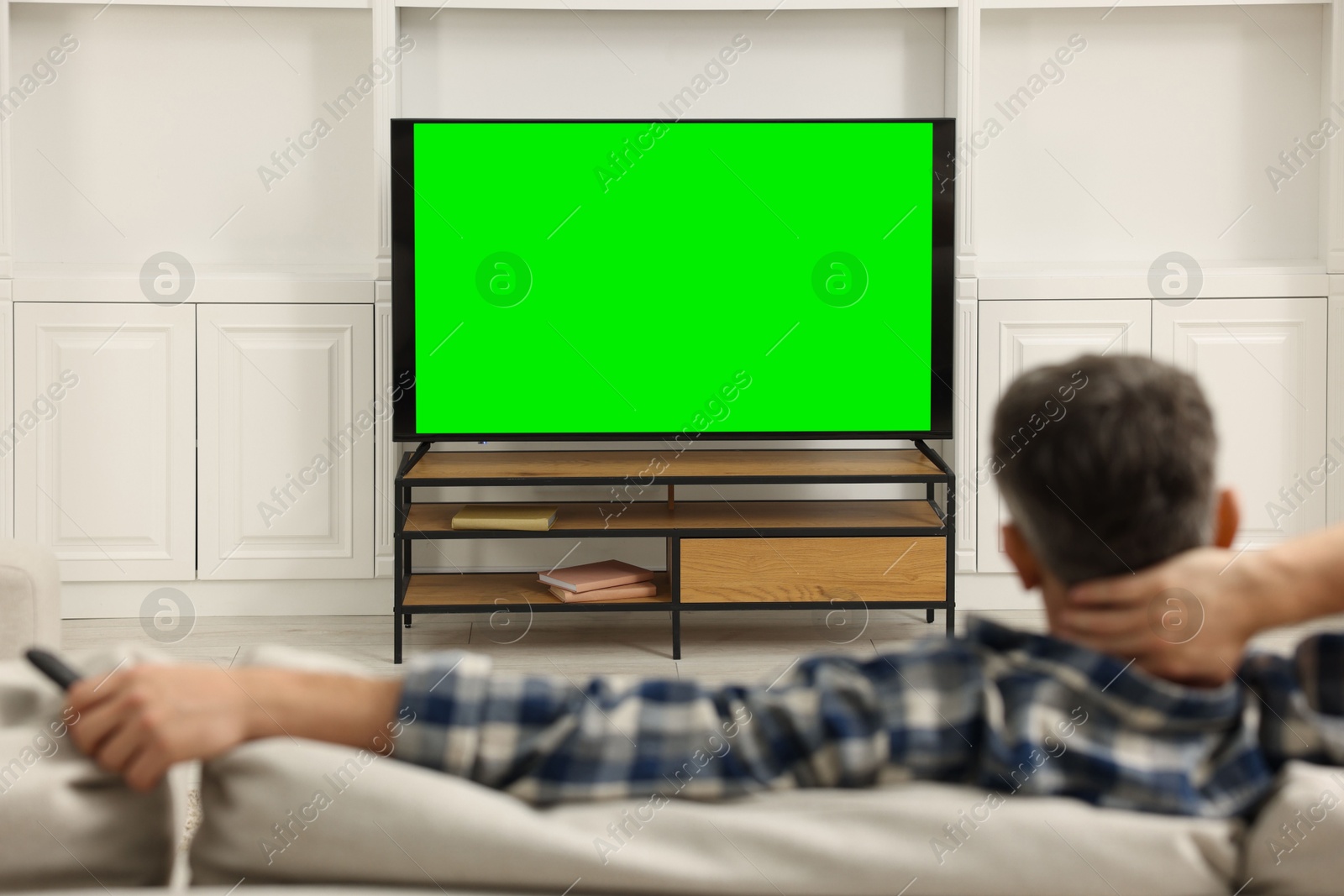 Photo of Man watching TV on sofa at home, back view